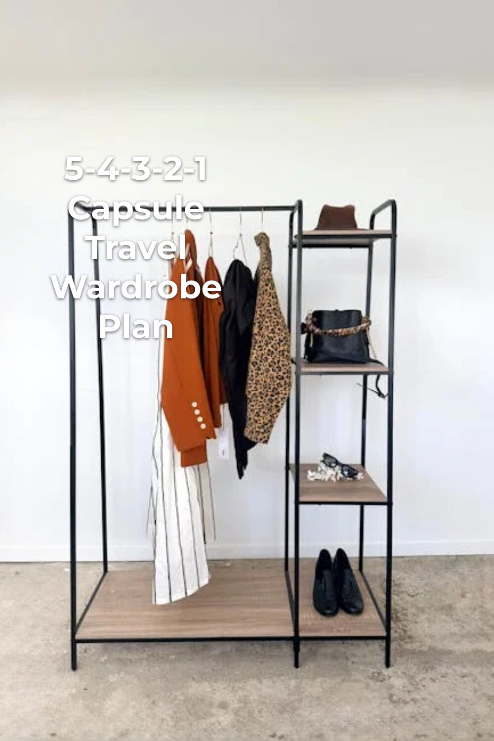 Capsule travel wardrobe on a black clothing rack with jackets, pants, hat, bag, jewelry, and shoes
