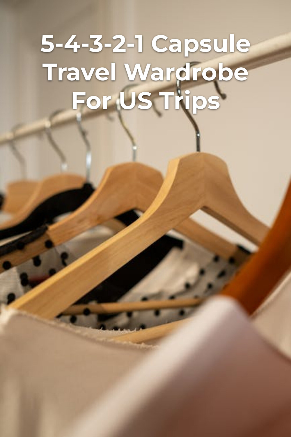 Capsule travel wardrobe on wooden hangers in a minimalist closet