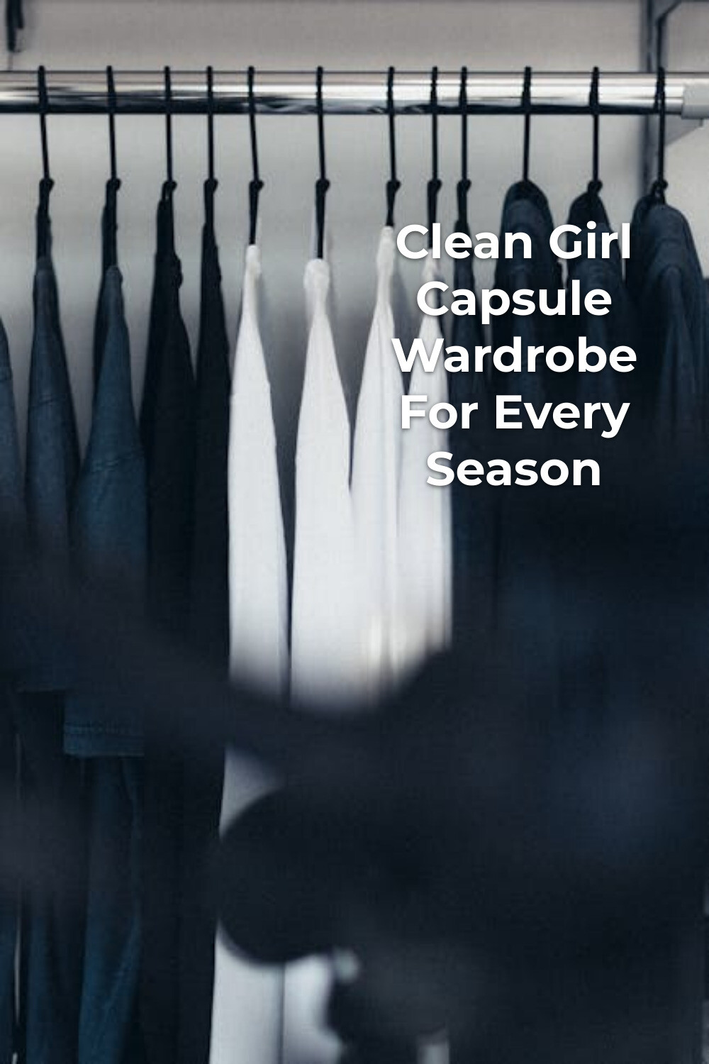 Clean girl capsule wardrobe with dark jackets and white shirts on a clothing rail, minimalist styling