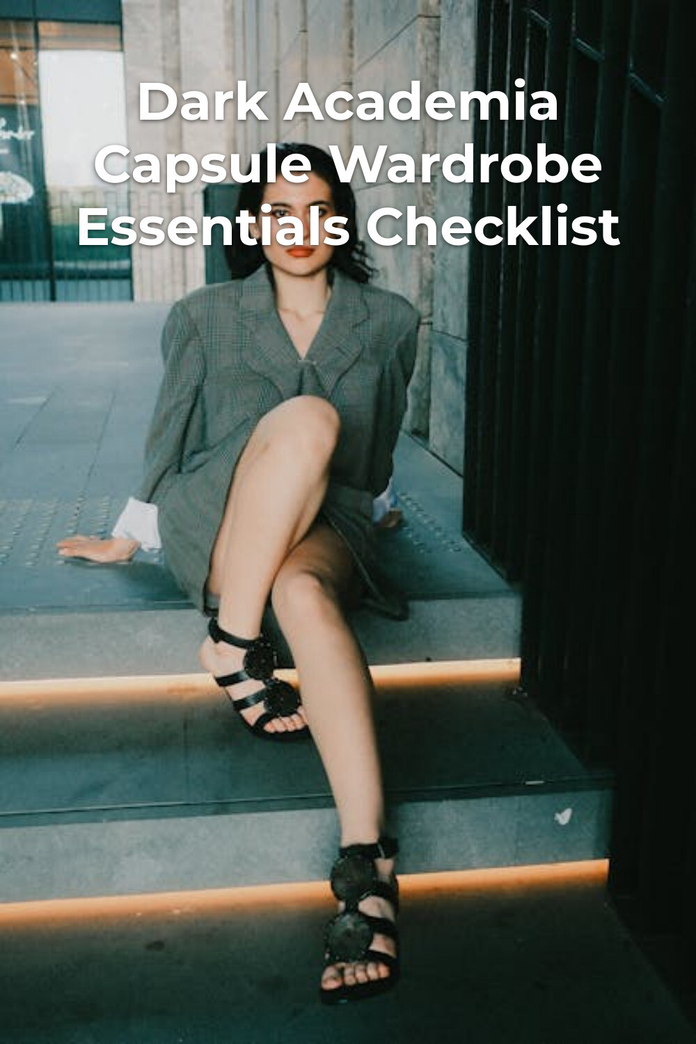 Dark academia capsule wardrobe look: woman in a gray blazer dress and black sandals sitting on stone steps