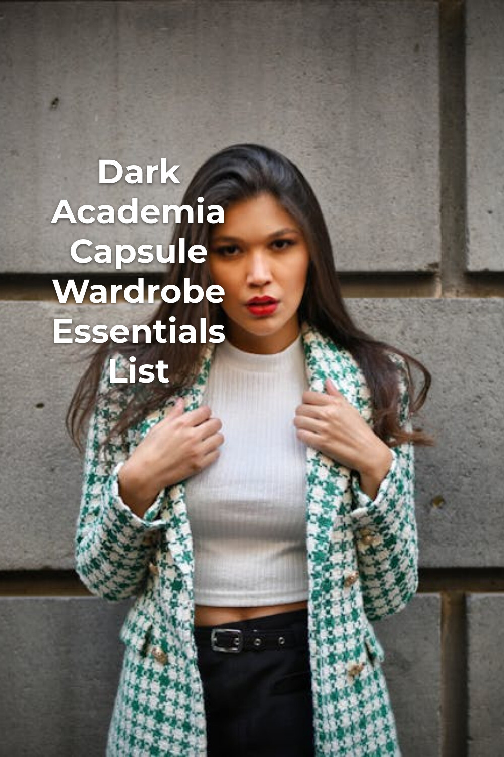 Dark academia capsule wardrobe look with woman in white top and patterned coat by a stone wall