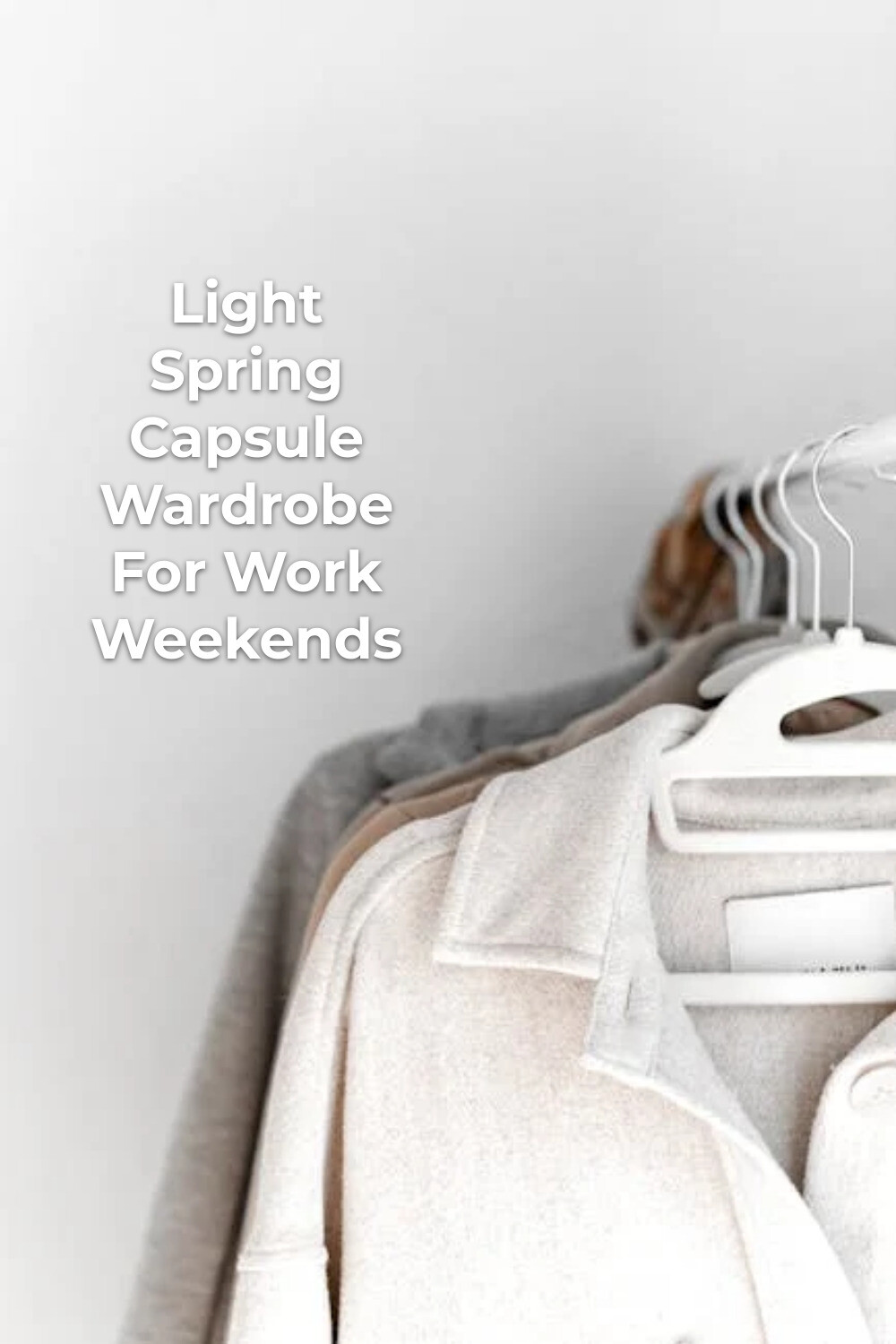 Light spring capsule wardrobe with light shirts on white hangers against a plain wall
