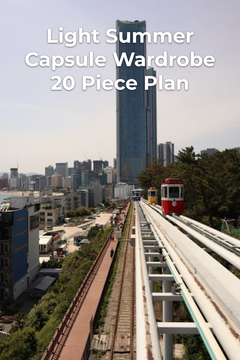 Red train on elevated track by glass tower, city skyline—light summer capsule wardrobe inspiration
